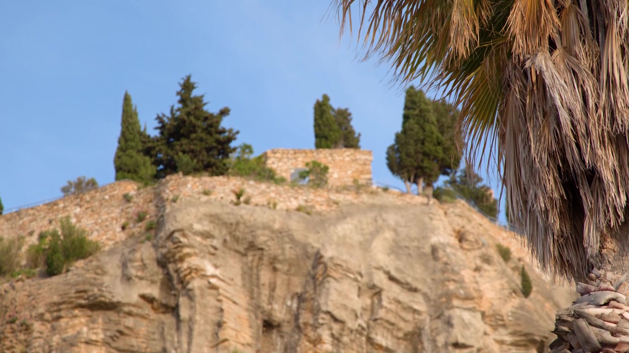 Ampia inquadratura statica di rovine storiche in pietra in cima a una scogliera rocciosa con alberi di cipresso