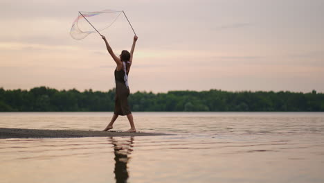 a young girl artist shows magic tricks using huge soap bubbles. create soap bubbles using sticks and rope at sunset to show a theatrical circus show