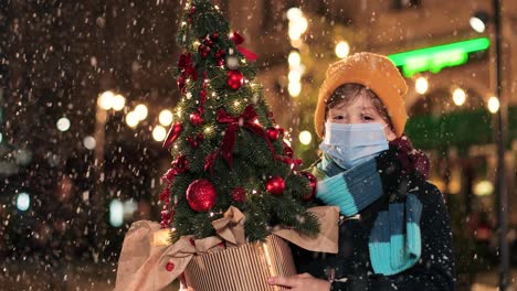 크리스마스에 거리에 눈이 내리는 동안 크리스마스 트리를 들고 카메라를 보고 웃는 행복한 백인 소년의 초상화