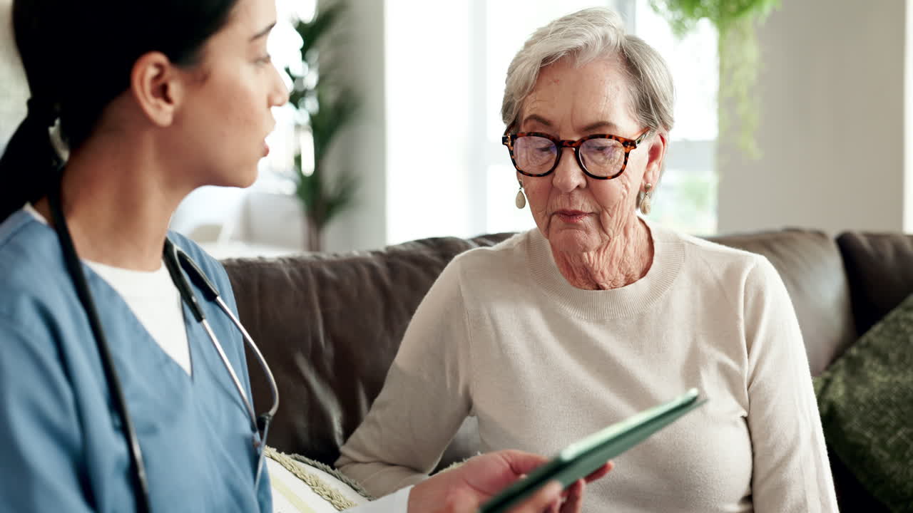 Nurse assisting elderly woman with tablet at home