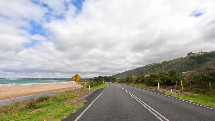 A serene drive along the Great Ocean Road with coastal views, lush greenery, and open skies under soft daylight