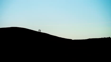 wide shot of silhouette of men doing topographic surveys on hill top