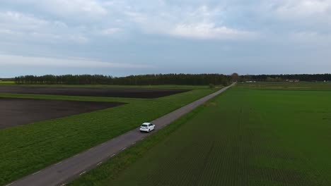 extreme wide aerial drone shot of a white car driving on a narrow country side road in south sweden skåne