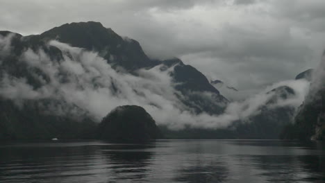 Slow-motion-pan-across-misty-and-cloudy-mountains-in-Doubtful-Sound-with-water-in-foreground---Patea,-New-Zealand