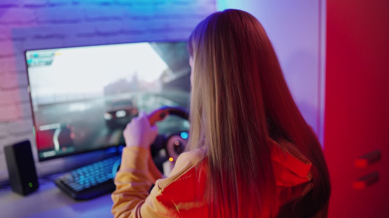 Long-haired girl playing video game. Back view of a young woman with steering wheel playing car racing on a computer at home. Gaming concept.