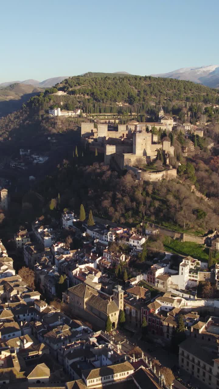 Voo aéreo frontal vertical sobre Granada, exibindo a paisagem urbana com a fortaleza de Alhambra erguendo-se ao fundo.