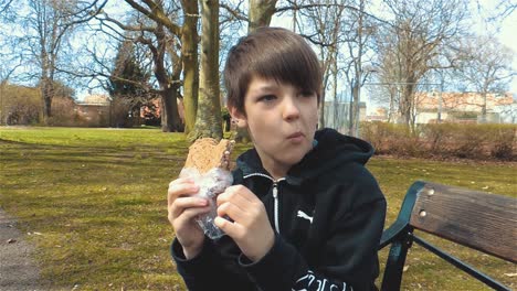 young caucasian boy eating sandwich outdoors drinking monster energy drink