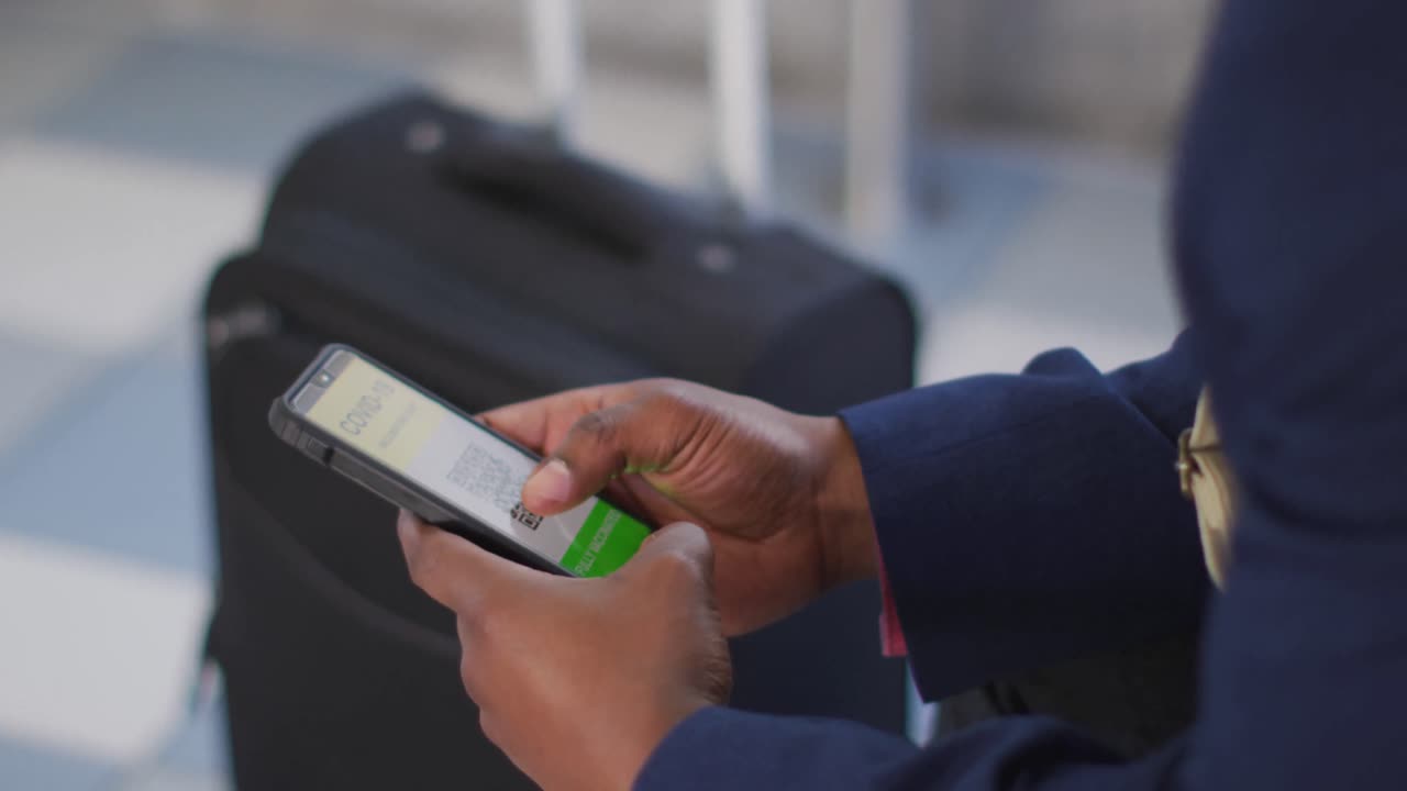 de manos hombre afroamericano en la ciudad usando un teléfono inteligente con pasaporte covid, esperando el autobús