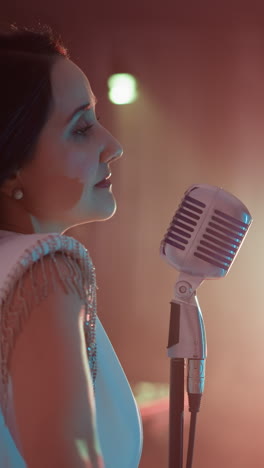 una cantante vestida con un vestido blanco se encuentra frente a un micrófono vintage, moviendo suavemente sus manos y cuerpo. la toma de ángulo lateral captura su gracia y expresividad