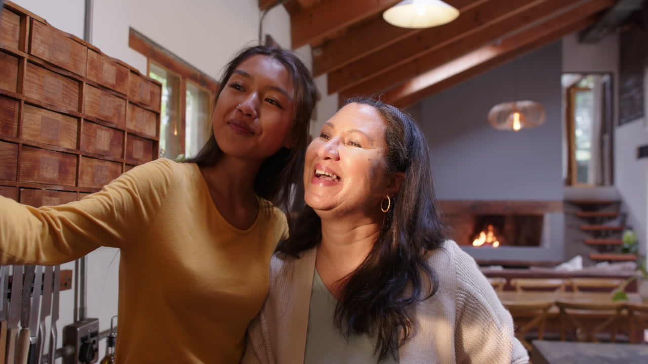 Multiracial young woman and multiracial grandma taking selfie together, smiling warmly at home