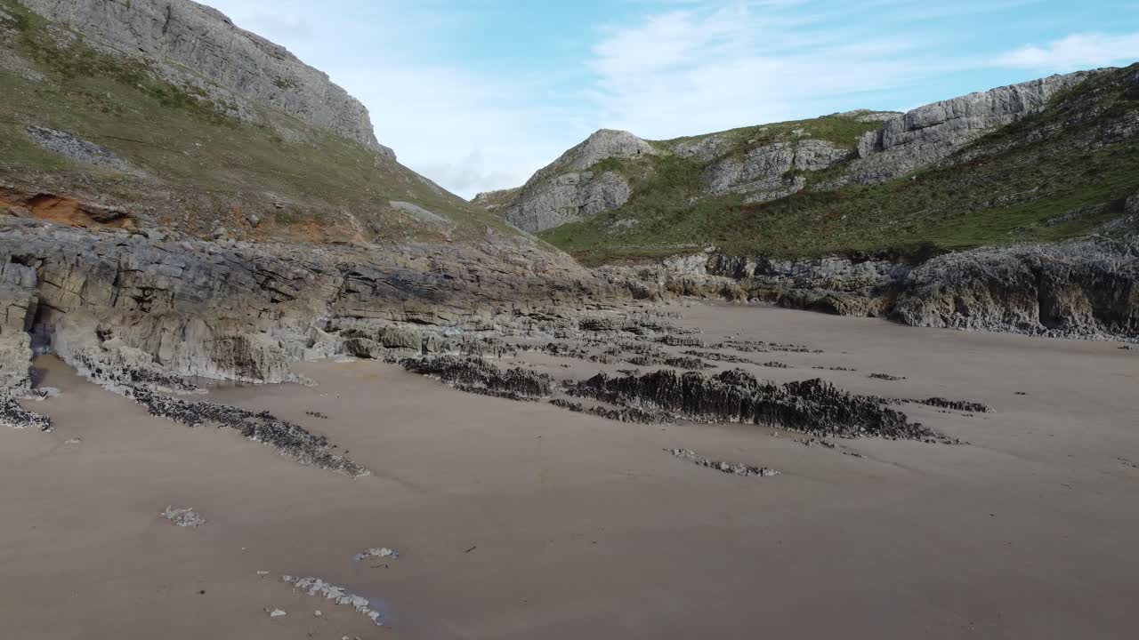 mewslade bay waes uk 4k의 바다 동굴과 황금빛 모래를 보여주는 계곡 입구에서 해변을 따라 후퇴하는 공중 드론 샷