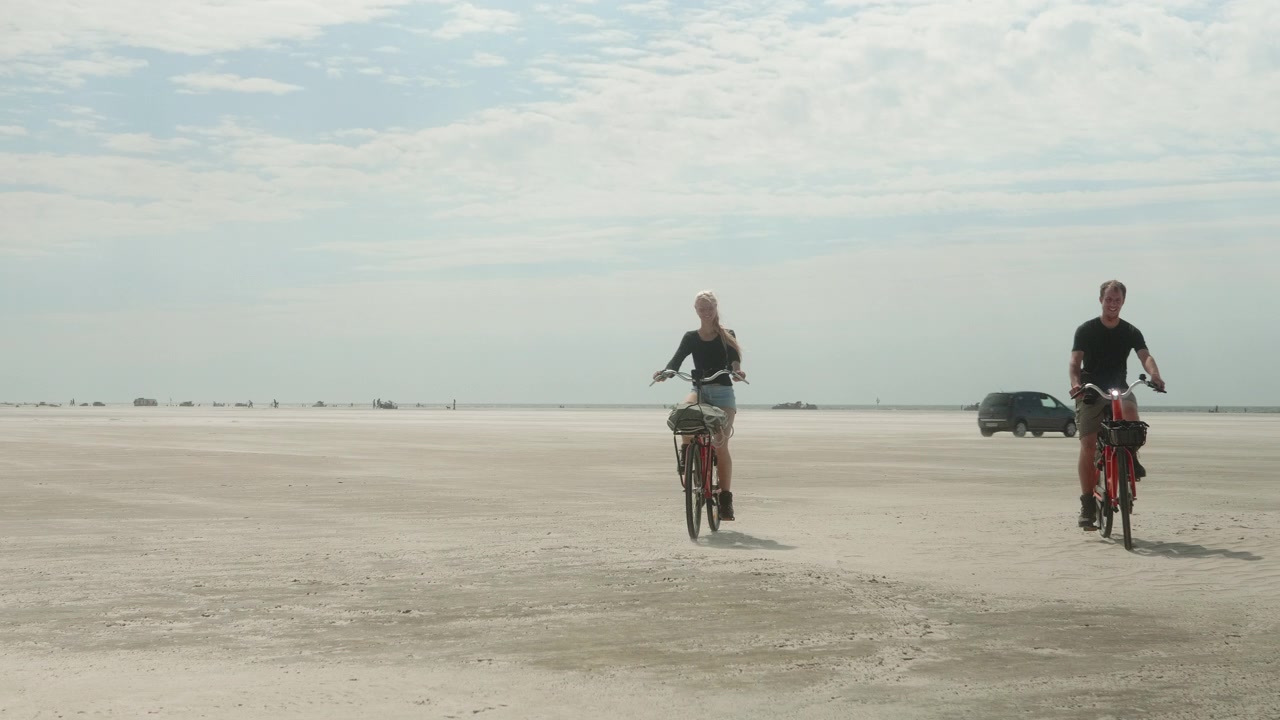 Giovane coppia che si avvicina alla telecamera con biciclette a noleggio sulla spiaggia in una soleggiata giornata estiva in Danimarca, spiaggia di Fanø, Esbjerg.