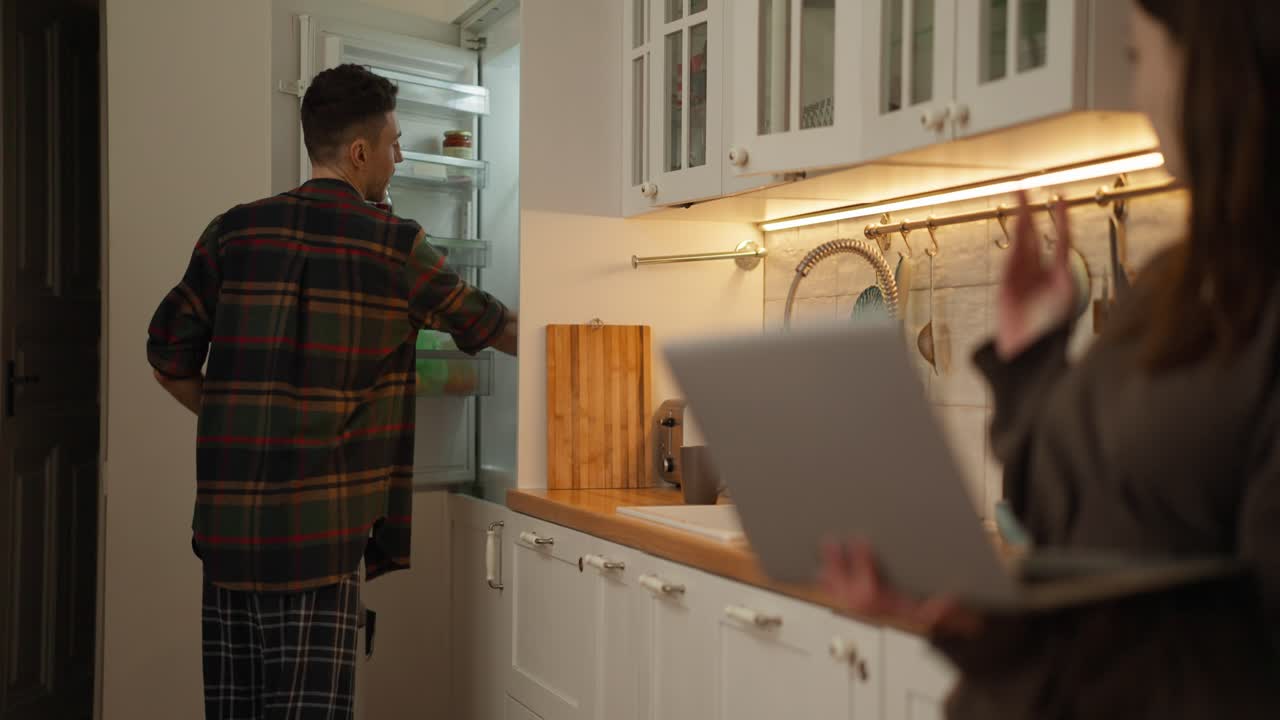 People in the kitchen with a refrigerator and laptop