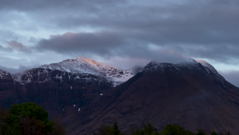 Scottish-Highlands-Time-Lapse,-snow-capped-Mountains-above-Invercoe,-Glencoe,-Scotland,-with-evening-sunlight-dappling-the-tops-of-the-mountains-and-mist-on-summit