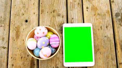 painted easter eggs in a bowl and digital tablet on wooden surface
