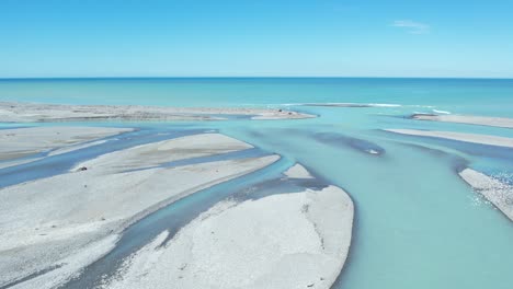 high aerial following main channel of beautiful turquoise-colored rakaia river as it exits into ocean