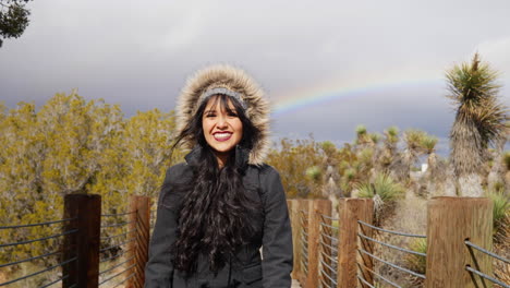 beautiful, happy young woman in a rain storm smiling with a colorful rainbow in the cloudy sky after bad weather slow motion