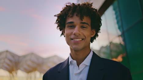 Hombre-De-Negocios-Sonriente-Posando-Retrato-De-La-Ciudad-Al-Atardecer.-Joven-Rizado-Mirando-La-Cámara