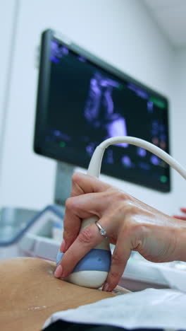 dark-haired female doctor checks the pregnant woman at ultrasound machine. medic mover the transducer by belly and looks at the monitor intently. low angle view.. vertical video
