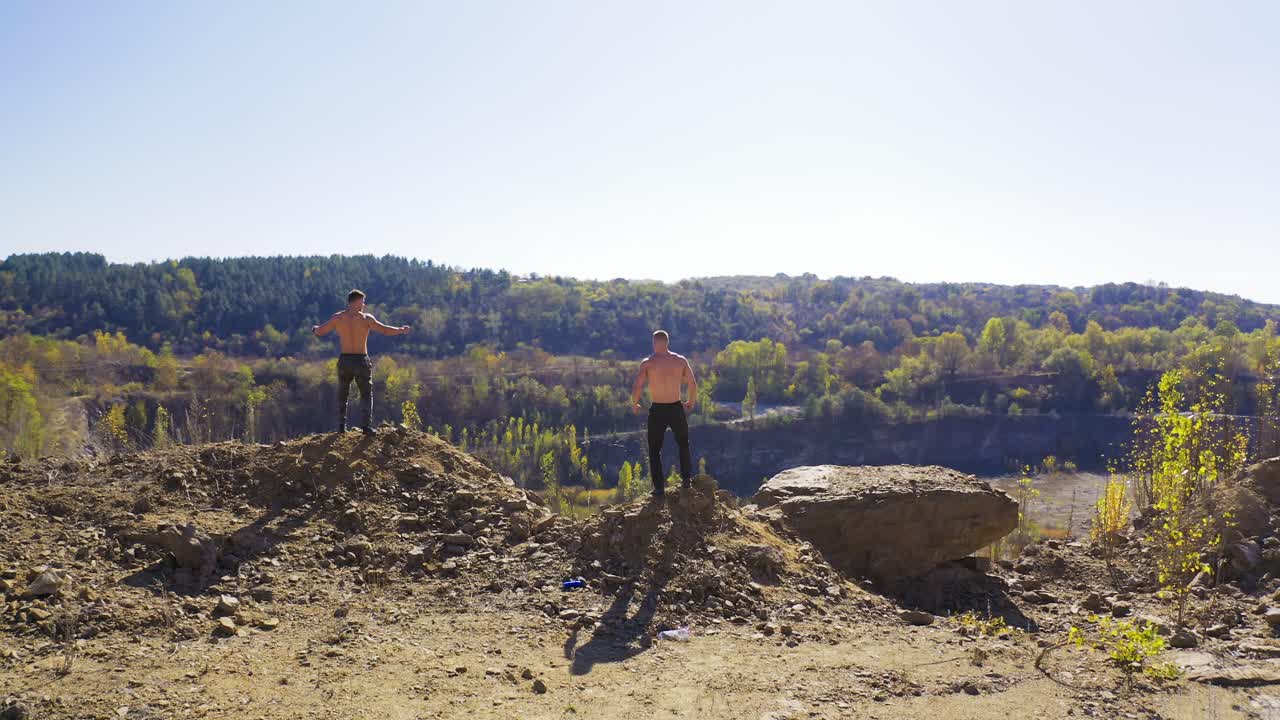 Backside view of two athletes training among nature. Sportive shirtless men with muscular body on the top of the hill. Aerial view.