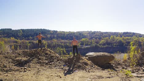 backside view of two athletes training among nature. sportive shirtless men with muscular body on the top of the hill. aerial view.