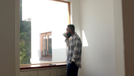 African-american-man-drinking-coffee-and-looking-out-window-at-home,-slow-motion