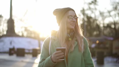 woman walking with hot drink by winter city park, enjoy weather