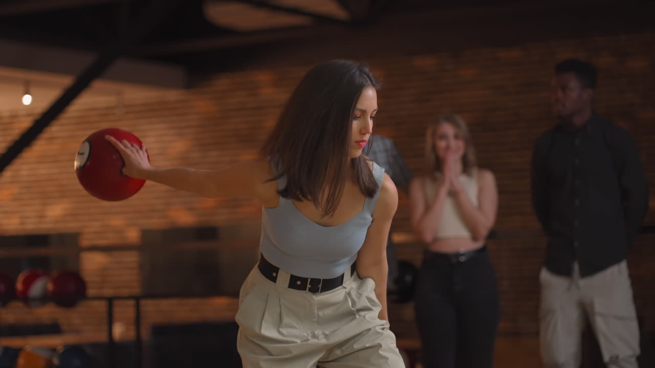 Portrait A young brunette woman makes the final throw with a bowling ball and wins the game with the support and joy of her friends of different nationalities. Rejoice and celebrate the victory