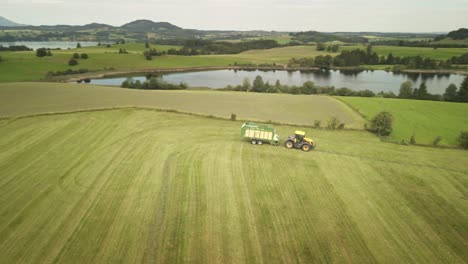 Drone captures a turning tractor in Allgäu, with a lake and the majestic Alps painting the perfect backdrop.
