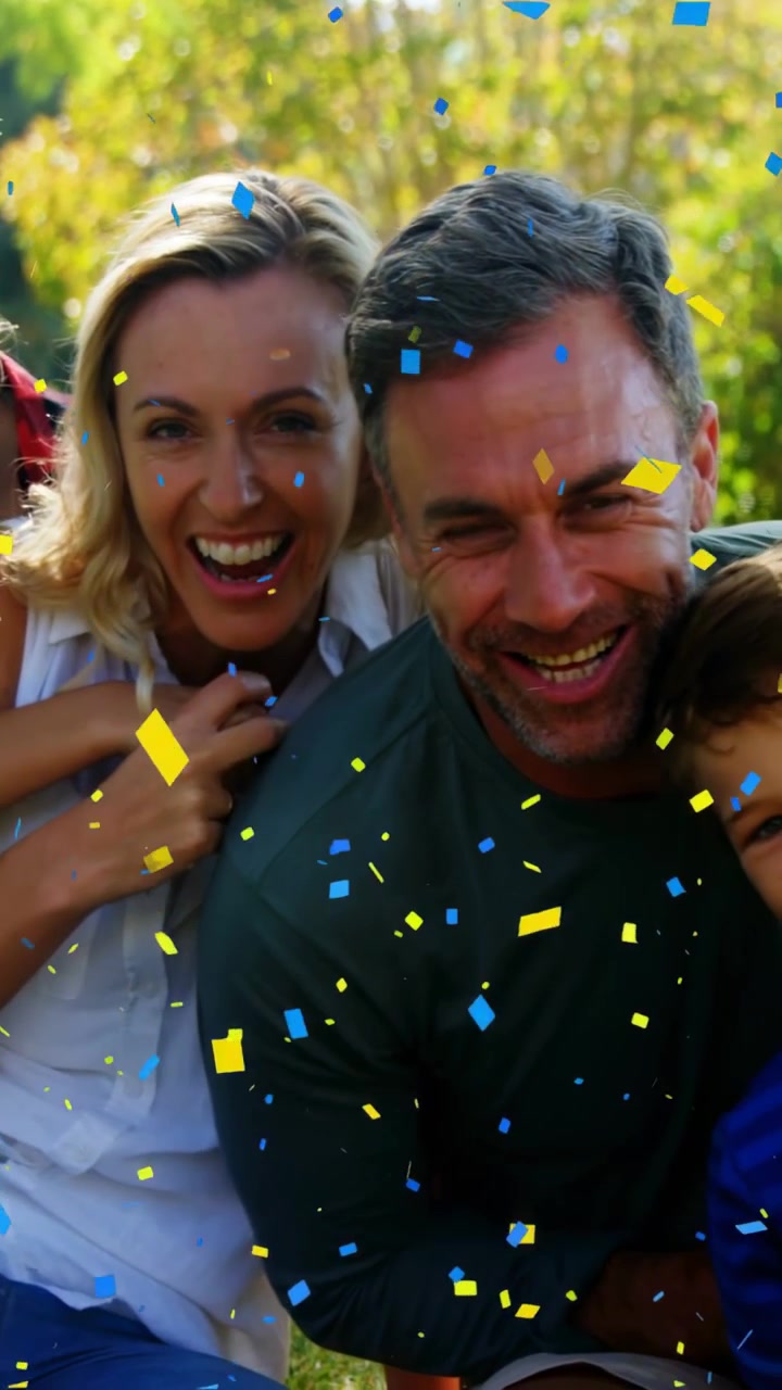 Video verticale: Carrellata all'indietro che mostra una famiglia su un prato, un bambino in spalla, coriandoli, festeggiamenti, marketing.