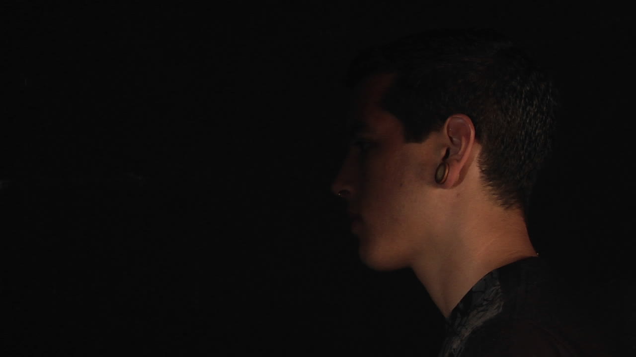 un hombre se para de perfil y luego se pone una máscara blanca en la cara