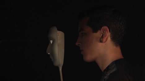 a man stands in profile then holds a white mask to his face