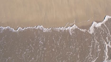 aerial top view of waves break on sand beach