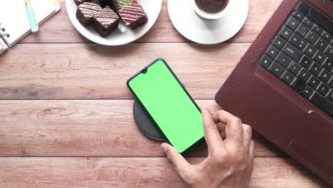 teléfono inteligente cargando inalámbricamente en un escritorio de madera con café, brownies y una computadora portátil