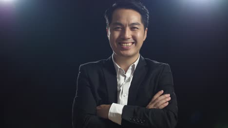 close up of smiling asian speaker man in business suit crossing his arms while standing in the black screen studio
