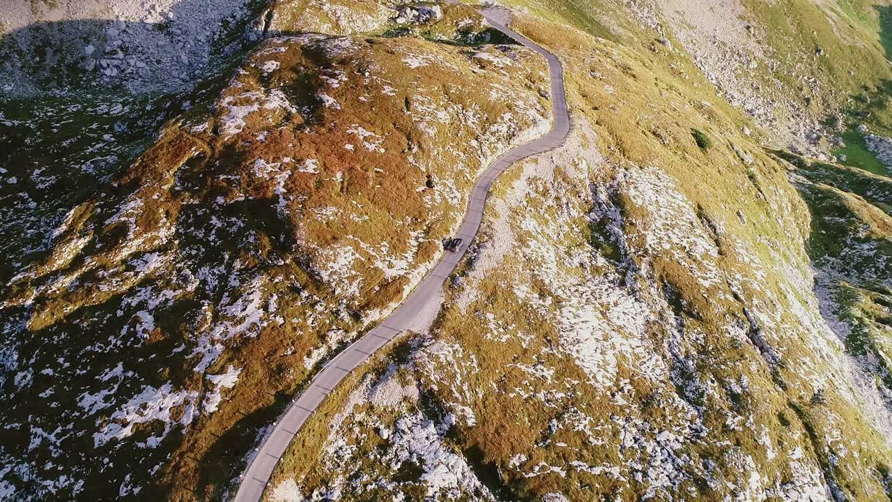 Vehicle follows narrow mountain road, Mangart Saddle during golden hour Slovenia