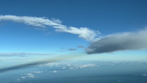 la perspectiva de un piloto volando en un cielo azul con algunas nubes esponjosas y sus sombras