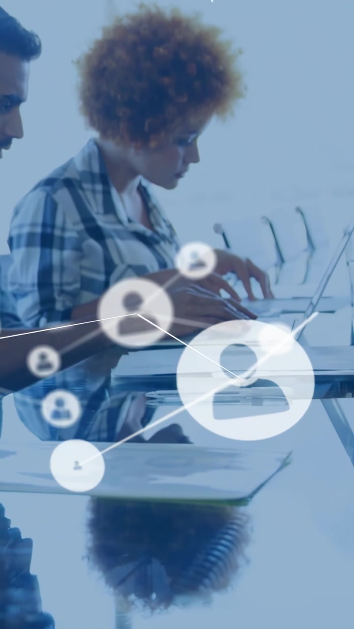 Vertical video: Woman typing on laptop initiating tech network overlay spreading across glass table