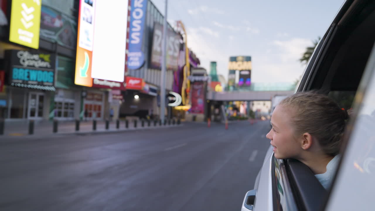 Young girl looking out car window on a busy city street