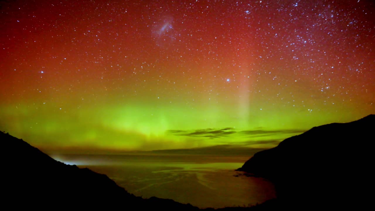 toma de timelapse que captura el fenómeno de la naturaleza, la aurora de la luz del sur ilumina el cielo nocturno, muestra patrones dinámicos de luces brillantes con colores rojo y verde en nugget point, nueva zelanda