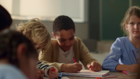 children sitting at round table in classroom. students drawing in notebooks