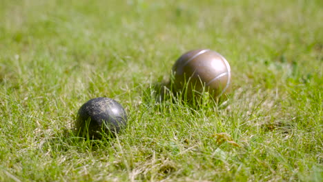 vue rapprochée de deux boules de pétanque en métal sur l'herbe, puis une autre boule s'écrase avec l'une d'elles