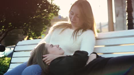 two women enjoying each other's company on a park bench in the sunshine