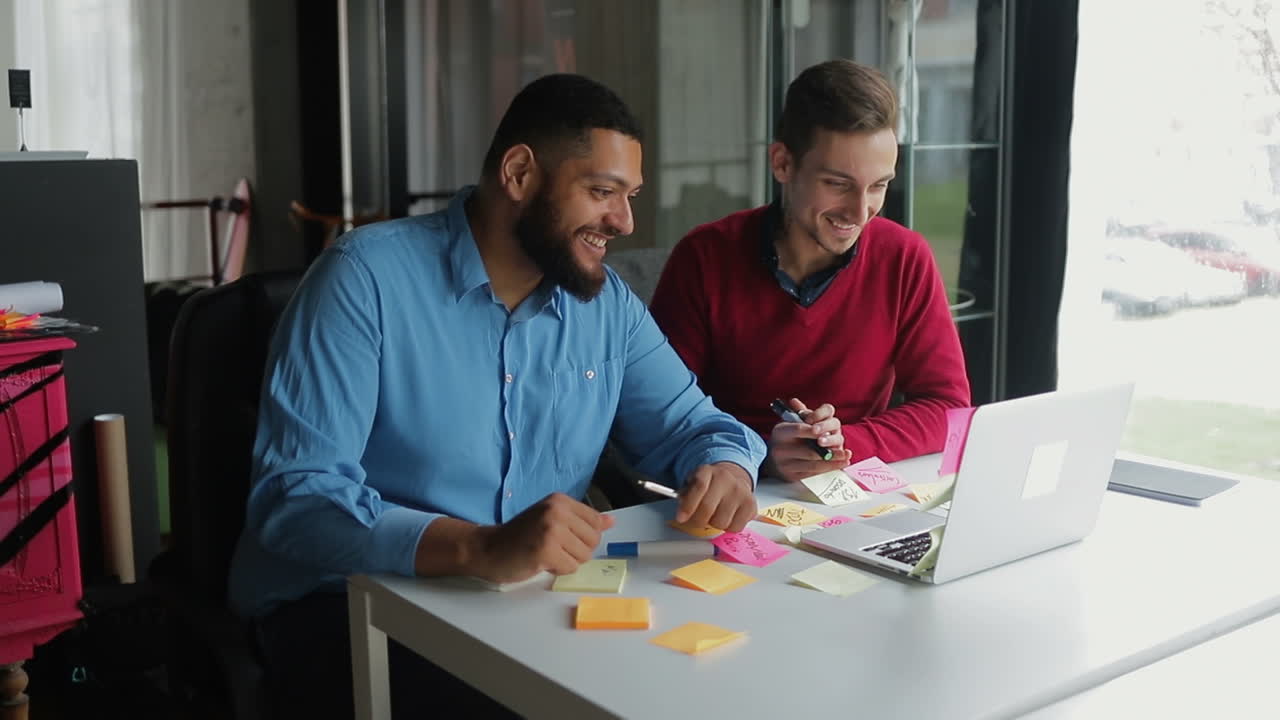 dos hombres jóvenes sonrientes saludando y hablando a la cámara.