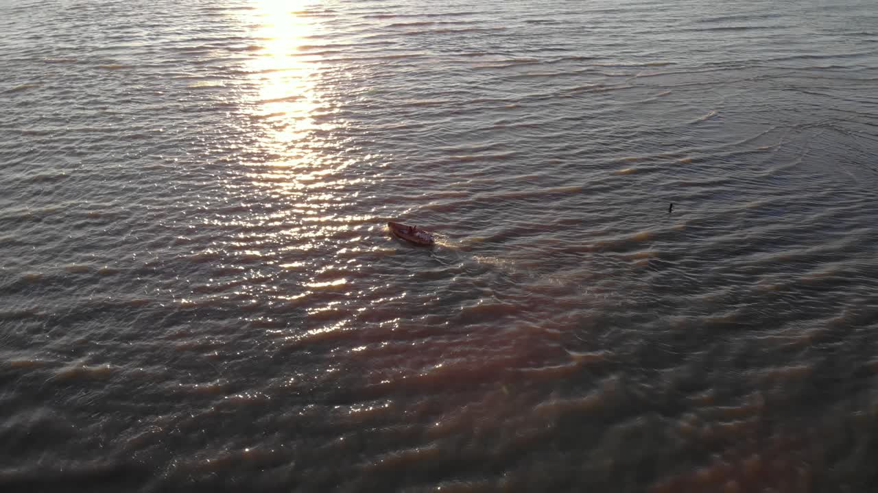 Fishing boat sailing through waves into open sea at evening with sun flares reflecting on vibrant water in Adriatic coast