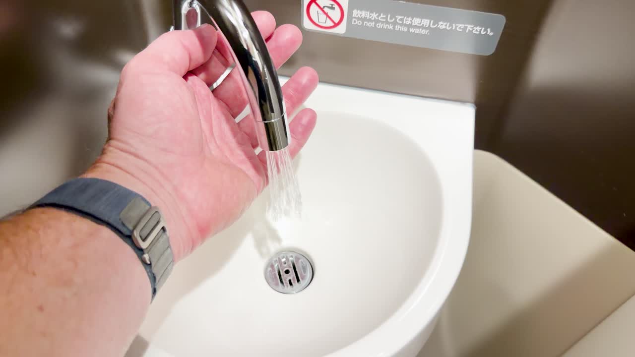 A person activates an automatic sensor faucet to wash their hands in a public restroom