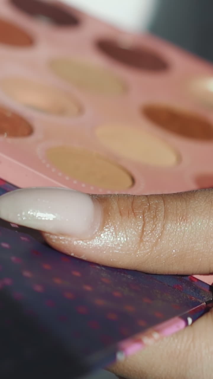 Makeup artist with dirty spot on hand holds palette with colorful eyeshadows working with client in beauty salon closeup. Professional decorative cosmetics