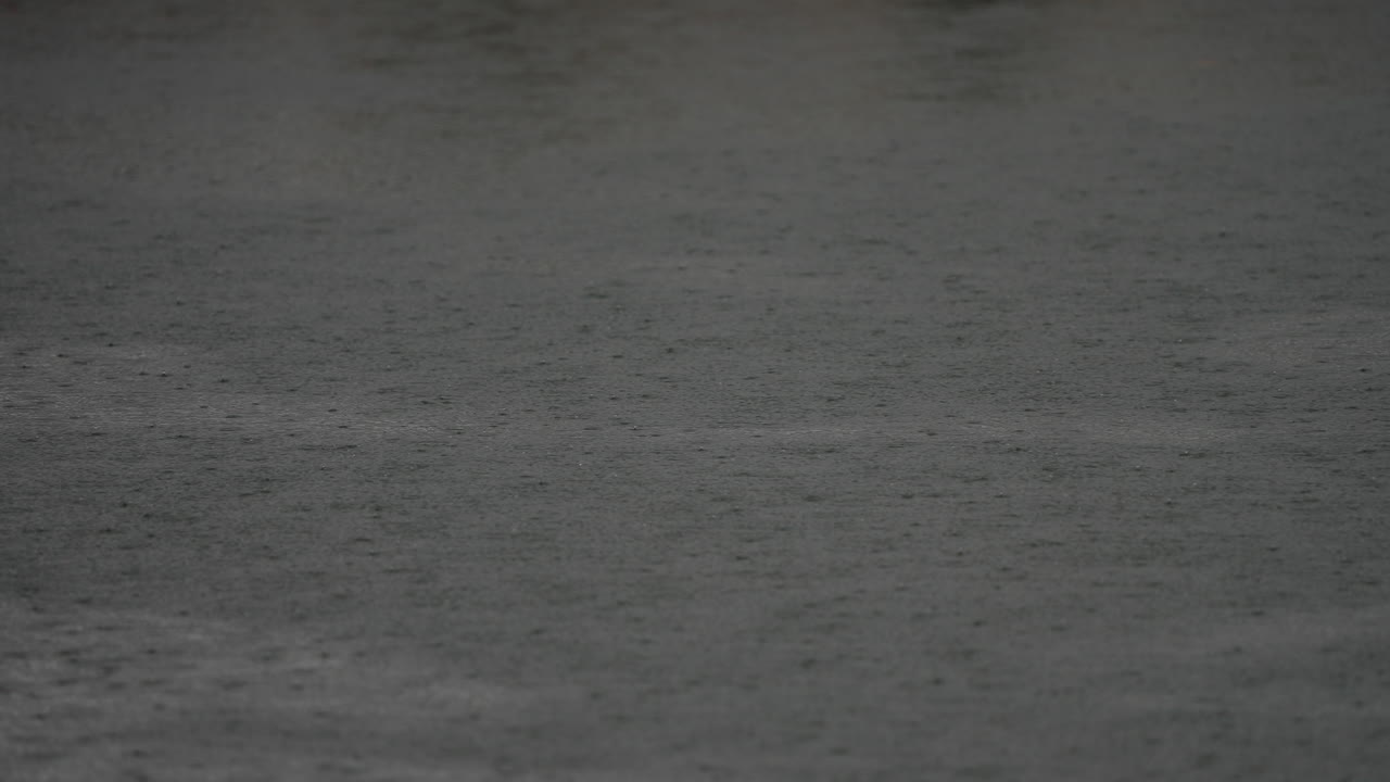 Dark water surface with rain falling, creating ripples and reflections, evoking a calm and serene atmosphere in nature