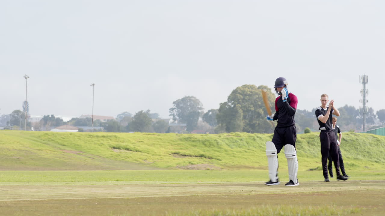 Two teams of multiracial male cricket players and male umpire playing cricket on pitch, copy space