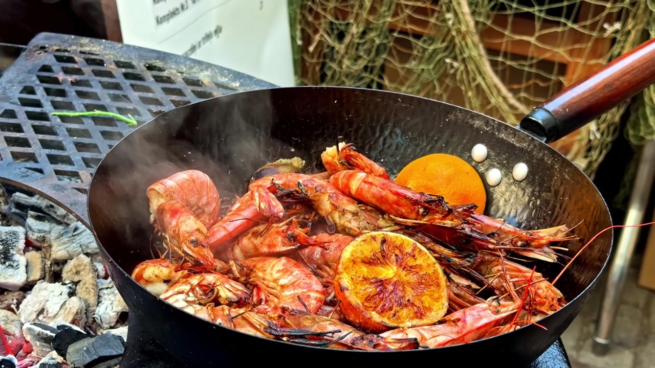 Shrimp are grilled in a wok on a barbecue together with orange slices.
